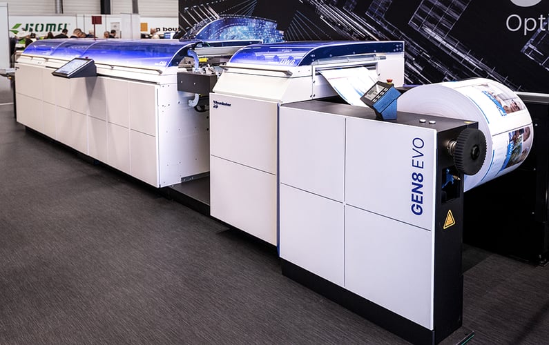 Hunkeler GEN8 EVO Produktionssystem auf Messeausstellung, verarbeitet große Papierrollen mit digitalem Hochgeschwindigkeitsdruck.