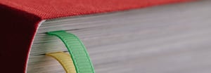 Nahaufnahme der Rückseite eines dicken Buches mit rotem Einband und zwei farbigen Lesebändchen, eines grün und eines gelb.