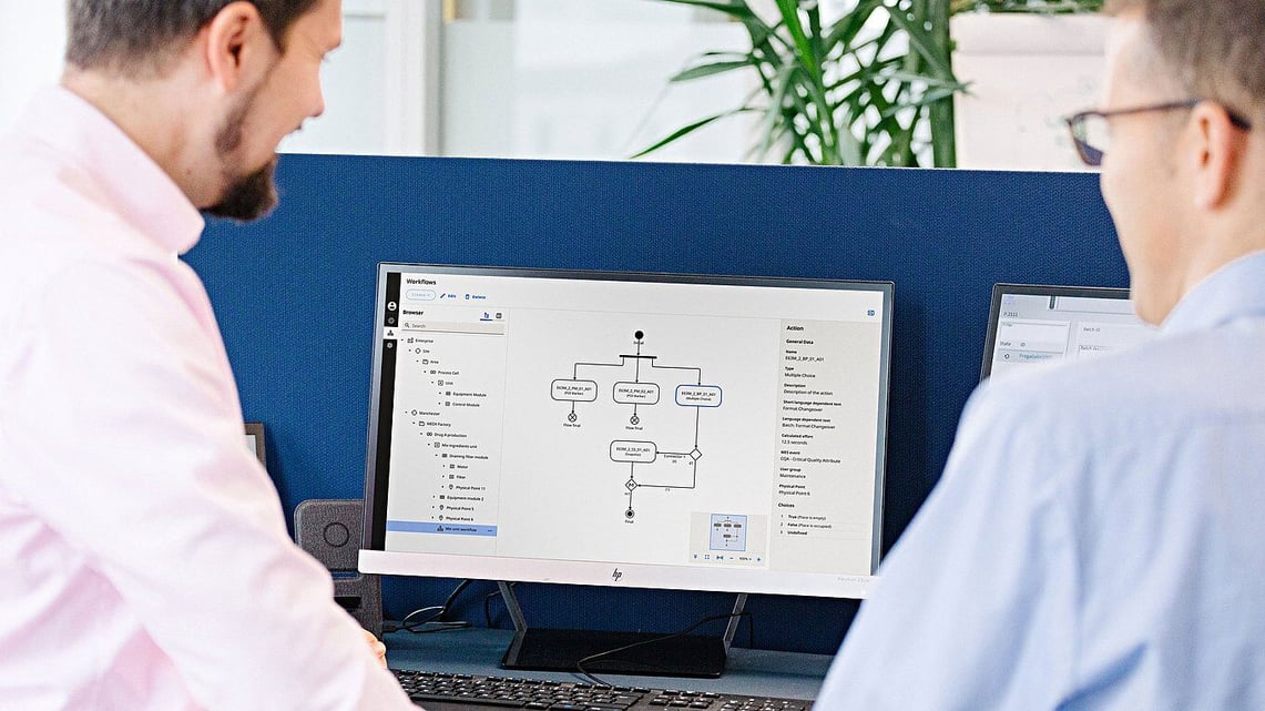 Two colleagues are looking at a workflow diagram on a computer screen in the office.